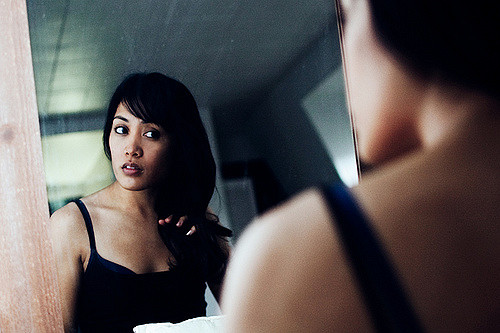 A woman looks at herself in the mirror with both hesitance and determination