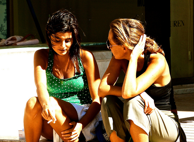 Two women sit on a ledge and talk.